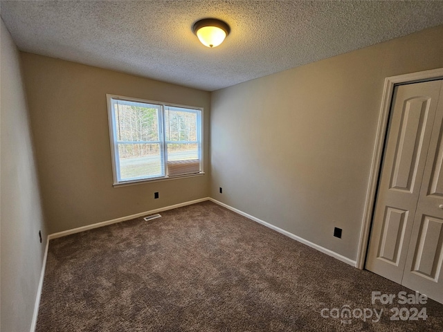 spare room featuring dark colored carpet and a textured ceiling