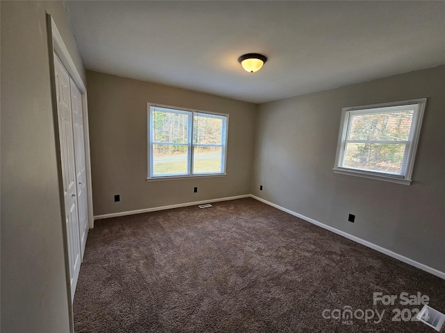 unfurnished bedroom featuring dark carpet, a closet, and multiple windows