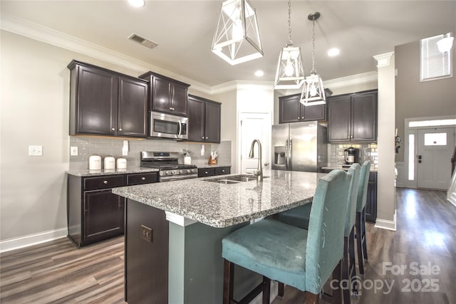 kitchen featuring appliances with stainless steel finishes, pendant lighting, sink, a kitchen bar, and a center island with sink