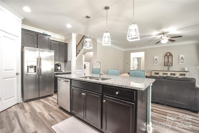 kitchen featuring sink, appliances with stainless steel finishes, hanging light fixtures, ornamental molding, and an island with sink