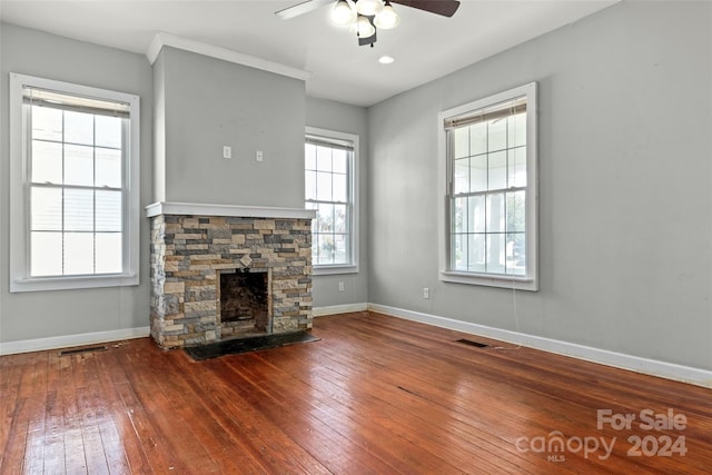 unfurnished living room with hardwood / wood-style floors, a stone fireplace, and ceiling fan