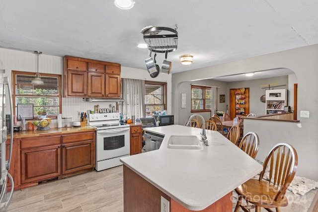 kitchen with electric stove, sink, hanging light fixtures, an island with sink, and tasteful backsplash