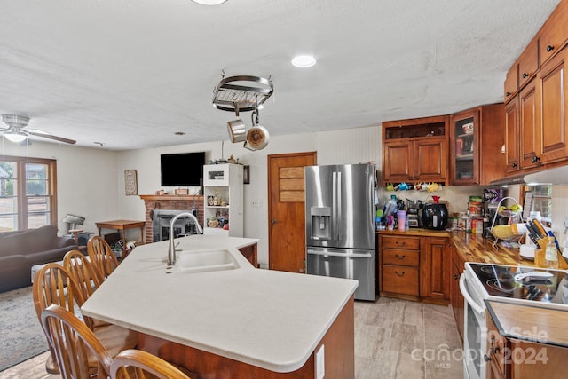 kitchen with ceiling fan, sink, white range with electric cooktop, stainless steel fridge, and a kitchen island with sink