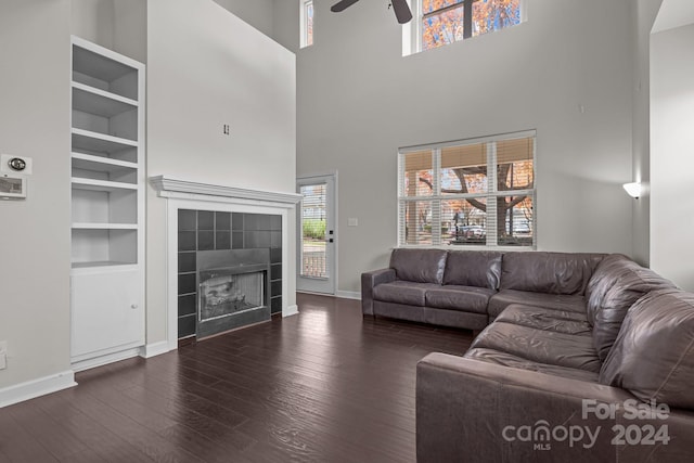 living room with a tile fireplace, a high ceiling, dark hardwood / wood-style floors, and ceiling fan