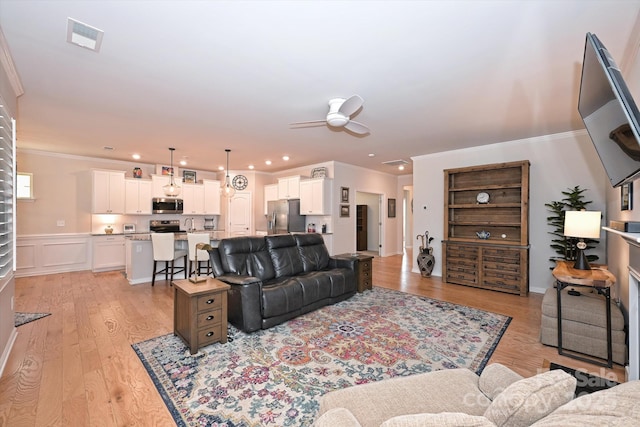 living room with crown molding, light hardwood / wood-style floors, and ceiling fan