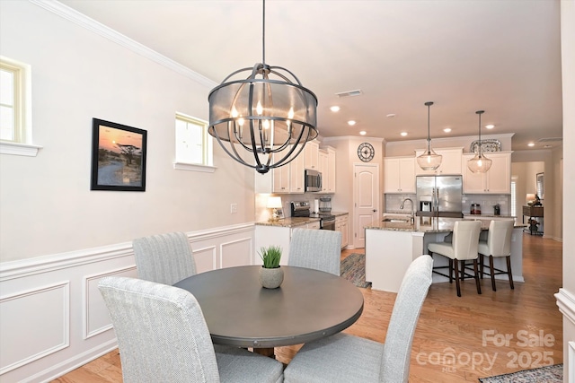 dining area with ornamental molding, sink, a notable chandelier, and light wood-type flooring