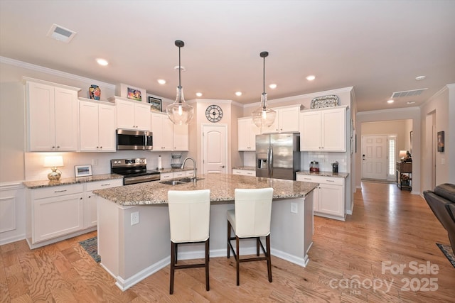 kitchen featuring sink, an island with sink, pendant lighting, stainless steel appliances, and white cabinets