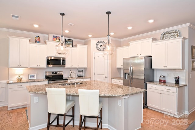 kitchen with hanging light fixtures, stainless steel appliances, an island with sink, and white cabinets