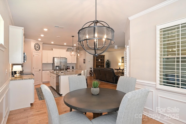 dining area with crown molding, sink, an inviting chandelier, and light hardwood / wood-style floors