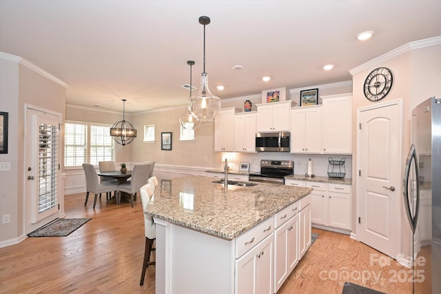 kitchen with appliances with stainless steel finishes, decorative light fixtures, sink, white cabinets, and a kitchen island with sink