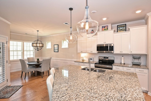 kitchen with appliances with stainless steel finishes, pendant lighting, sink, white cabinets, and crown molding