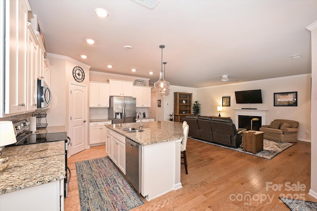 kitchen featuring decorative light fixtures, an island with sink, white cabinets, and appliances with stainless steel finishes