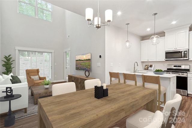 dining area featuring sink, dark wood-type flooring, a high ceiling, and a notable chandelier