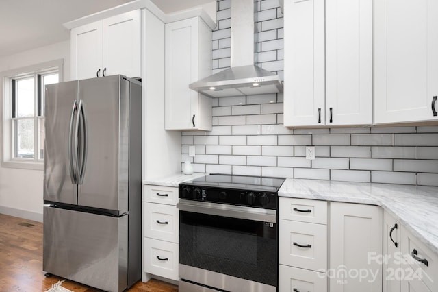 kitchen with wall chimney range hood, light stone countertops, appliances with stainless steel finishes, light hardwood / wood-style floors, and white cabinetry