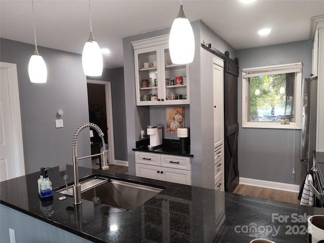 kitchen with dark stone counters, sink, a barn door, white cabinetry, and hanging light fixtures