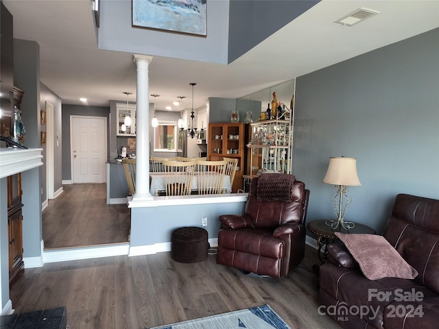 living room featuring decorative columns, dark wood-type flooring, and an inviting chandelier