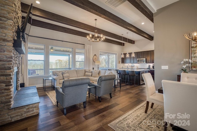 living room featuring beamed ceiling, ceiling fan with notable chandelier, dark hardwood / wood-style floors, and a stone fireplace