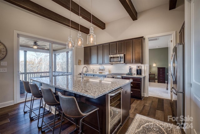 kitchen with appliances with stainless steel finishes, dark hardwood / wood-style flooring, beverage cooler, sink, and an island with sink