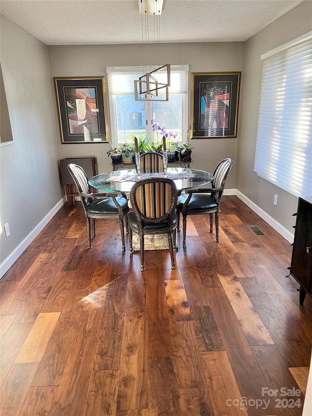 dining area with wood-type flooring, a textured ceiling, and an inviting chandelier