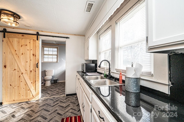 kitchen featuring a textured ceiling, a barn door, white cabinetry, and sink