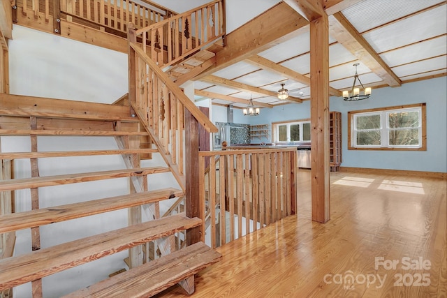 stairs featuring ceiling fan with notable chandelier, vaulted ceiling with beams, and hardwood / wood-style floors