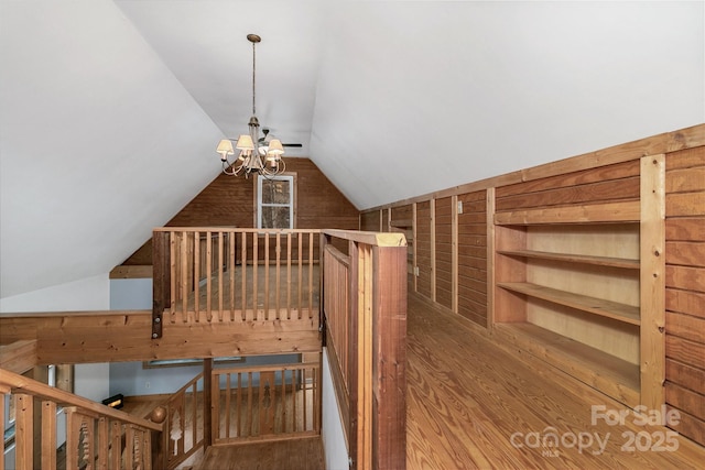 bonus room with built in shelves, lofted ceiling, an inviting chandelier, and wood-type flooring