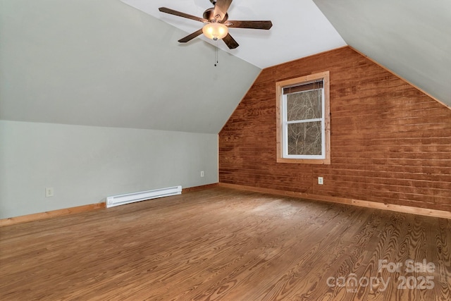 additional living space featuring wood walls, wood-type flooring, vaulted ceiling, a baseboard radiator, and ceiling fan