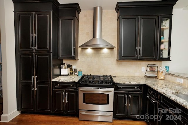 kitchen featuring decorative backsplash, light stone counters, wall chimney exhaust hood, hardwood / wood-style flooring, and stainless steel range with gas stovetop