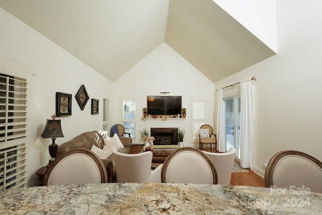 dining room featuring plenty of natural light, light wood-type flooring, a fireplace, and high vaulted ceiling