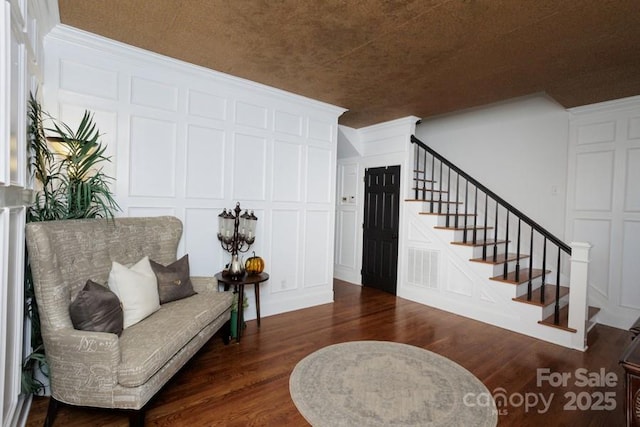 sitting room with stairs, dark wood-type flooring, visible vents, and a decorative wall