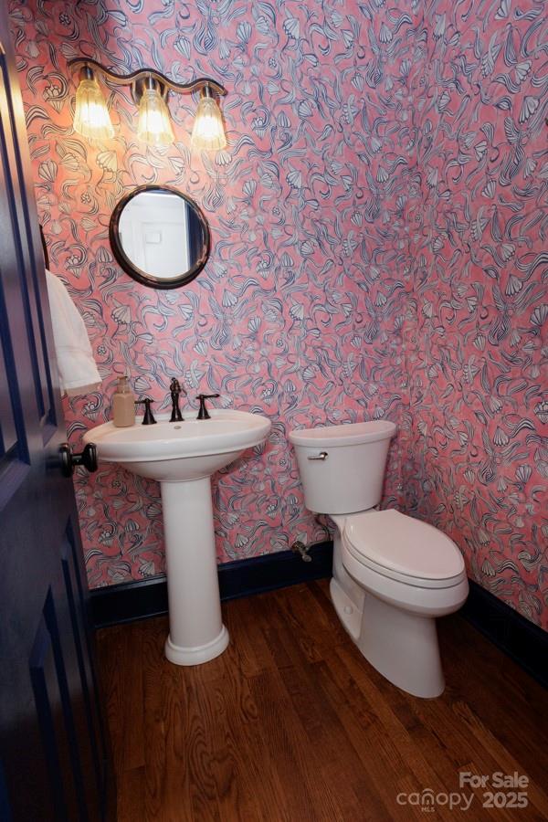 half bathroom with toilet, wallpapered walls, baseboards, and wood finished floors