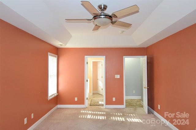 unfurnished bedroom featuring a tray ceiling, light carpet, and ceiling fan