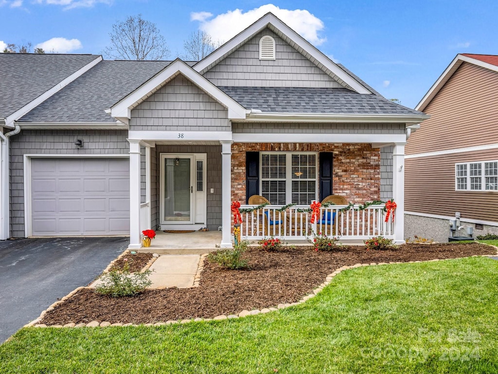 view of front facade featuring covered porch, a front yard, and a garage