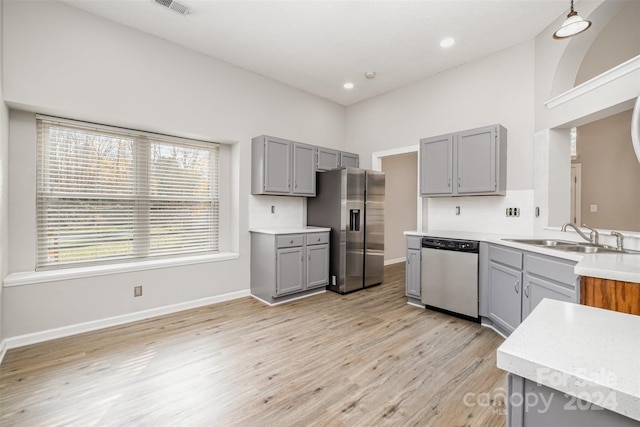 kitchen with gray cabinetry, sink, light wood-type flooring, appliances with stainless steel finishes, and tasteful backsplash