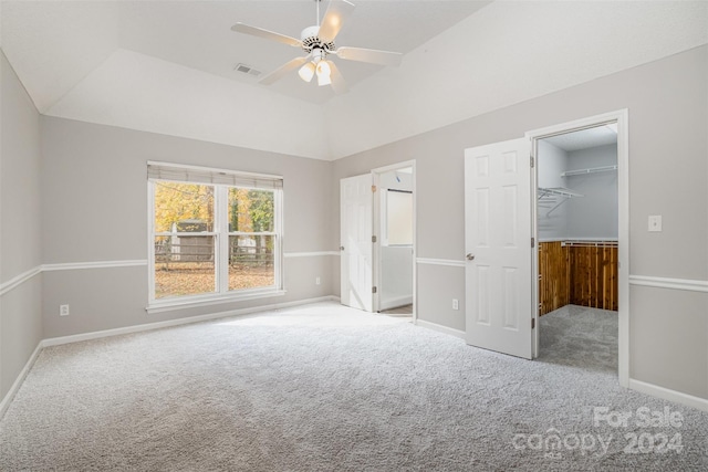 unfurnished bedroom with light carpet, a walk in closet, ceiling fan, a closet, and lofted ceiling