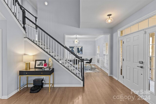 entryway with a wealth of natural light, crown molding, wood-type flooring, and an inviting chandelier