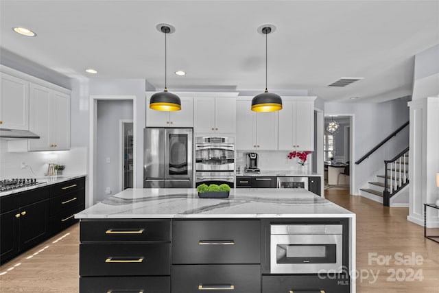 kitchen with decorative light fixtures, a center island, stainless steel appliances, and white cabinetry