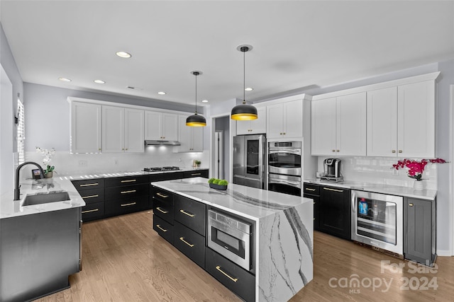 kitchen with appliances with stainless steel finishes, beverage cooler, sink, pendant lighting, and white cabinets