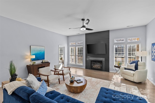 living room with hardwood / wood-style floors, a large fireplace, and ceiling fan