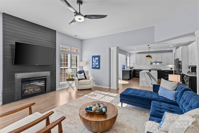 living room featuring a large fireplace, light hardwood / wood-style flooring, and ceiling fan