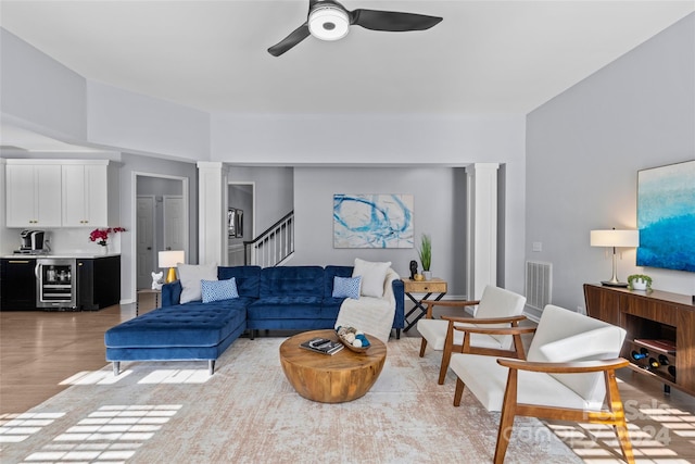 living room featuring wine cooler, ceiling fan, ornate columns, and hardwood / wood-style flooring