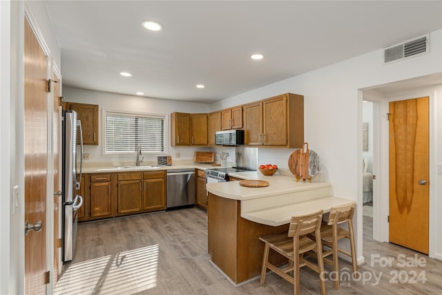 kitchen featuring sink, a kitchen breakfast bar, light hardwood / wood-style flooring, kitchen peninsula, and appliances with stainless steel finishes