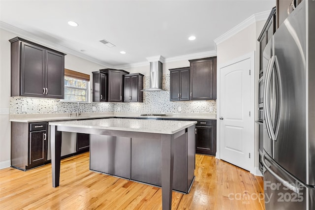 kitchen featuring light hardwood / wood-style floors, a kitchen island, appliances with stainless steel finishes, wall chimney exhaust hood, and dark brown cabinets