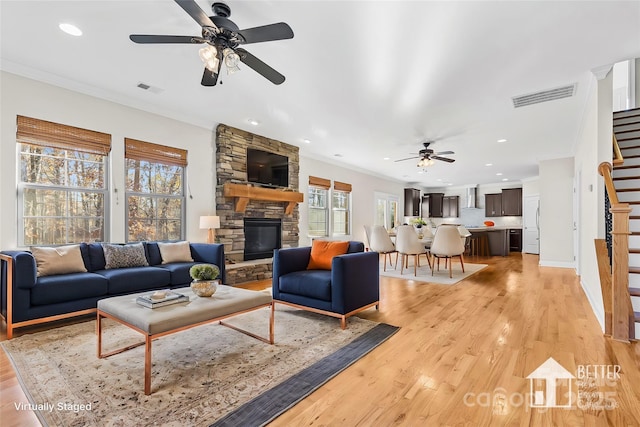 living room featuring ceiling fan, light wood-type flooring, a fireplace, and crown molding