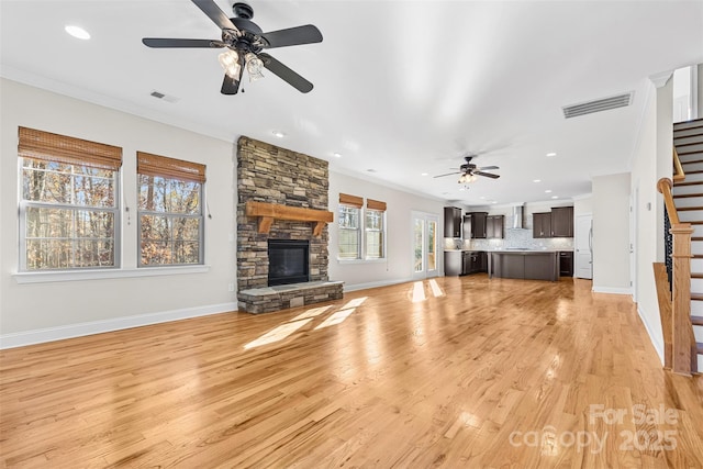 unfurnished living room featuring light wood-type flooring, ceiling fan, ornamental molding, and a stone fireplace