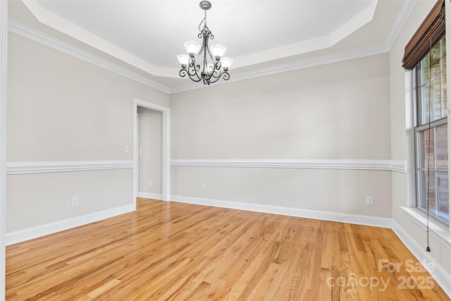 empty room with plenty of natural light, light hardwood / wood-style flooring, a raised ceiling, and a notable chandelier