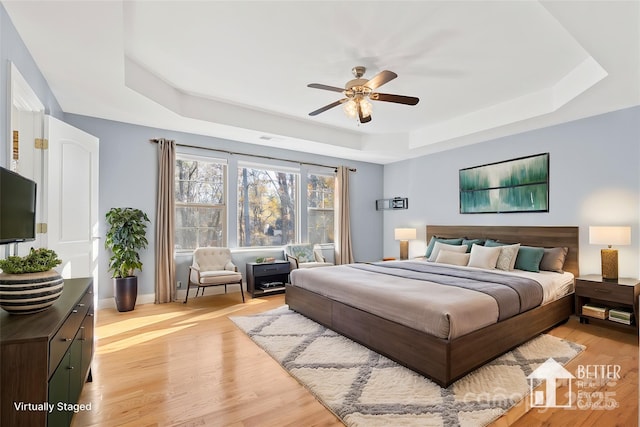 bedroom featuring a raised ceiling, ceiling fan, and light wood-type flooring