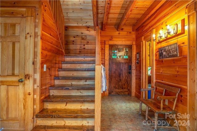 stairs featuring wood walls, beam ceiling, and wooden ceiling