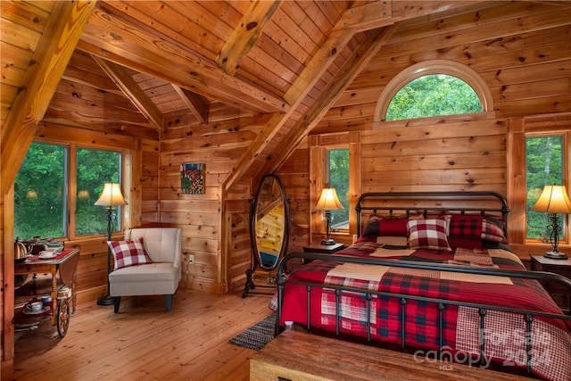 bedroom with vaulted ceiling with beams, light wood-type flooring, and wooden walls