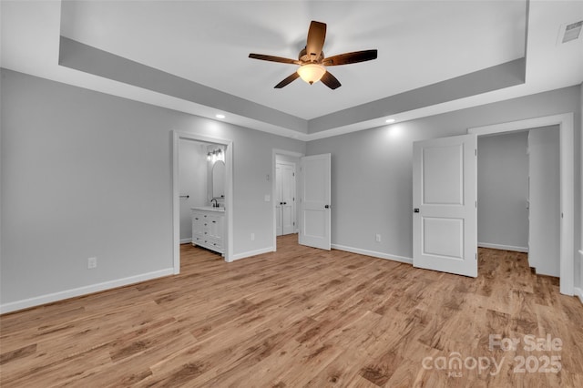 unfurnished bedroom with connected bathroom, baseboards, light wood-type flooring, recessed lighting, and a raised ceiling